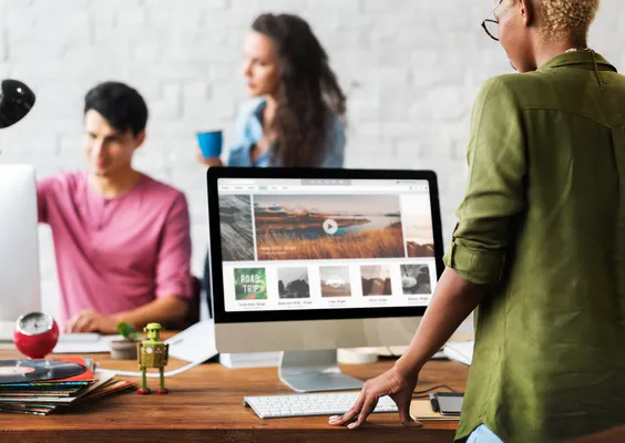 Grupo de personas trabajando en equipo con laptops y pantallas digitales, colaborando en el rediseño de sitio web con herramientas modernas.