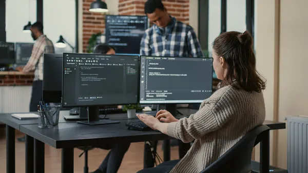 Mujer sentada frente a computadoras en una oficina va a comprar dominio web