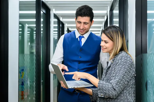 Un hombre vestido de traje y una mujer sostienen una computadora evaluando el hosting Mexico