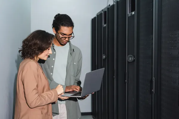 Una mujer y un joven que sostiene una computadora, evalúan la mejor opción de hosting México