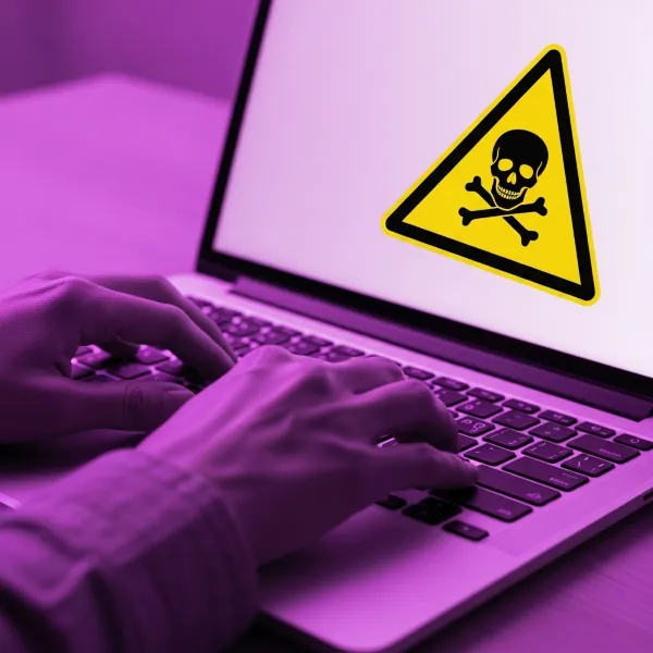 Persona escribiendo en un laptop con alerta de calavera, un caso de cómo limpiar tu hosting si tienes malware o virus.